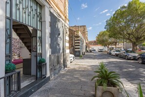 A street view with parked cars, a staircase leading to a building, and a tree-lined sidewalk.