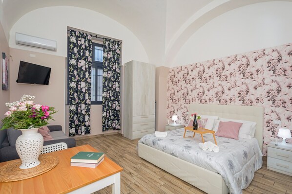 A bedroom with a bed, bedside table, TV, wardrobe, and floral wallpaper.