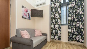 A room with a grey sofa, a flat-screen TV, floral curtains, and a wooden floor.