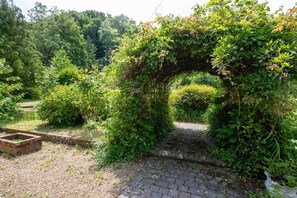 A brick pathway leading through a lush garden with a brick-built archway. - Eastwoods Cottage - Winchelsea (East Sussex)