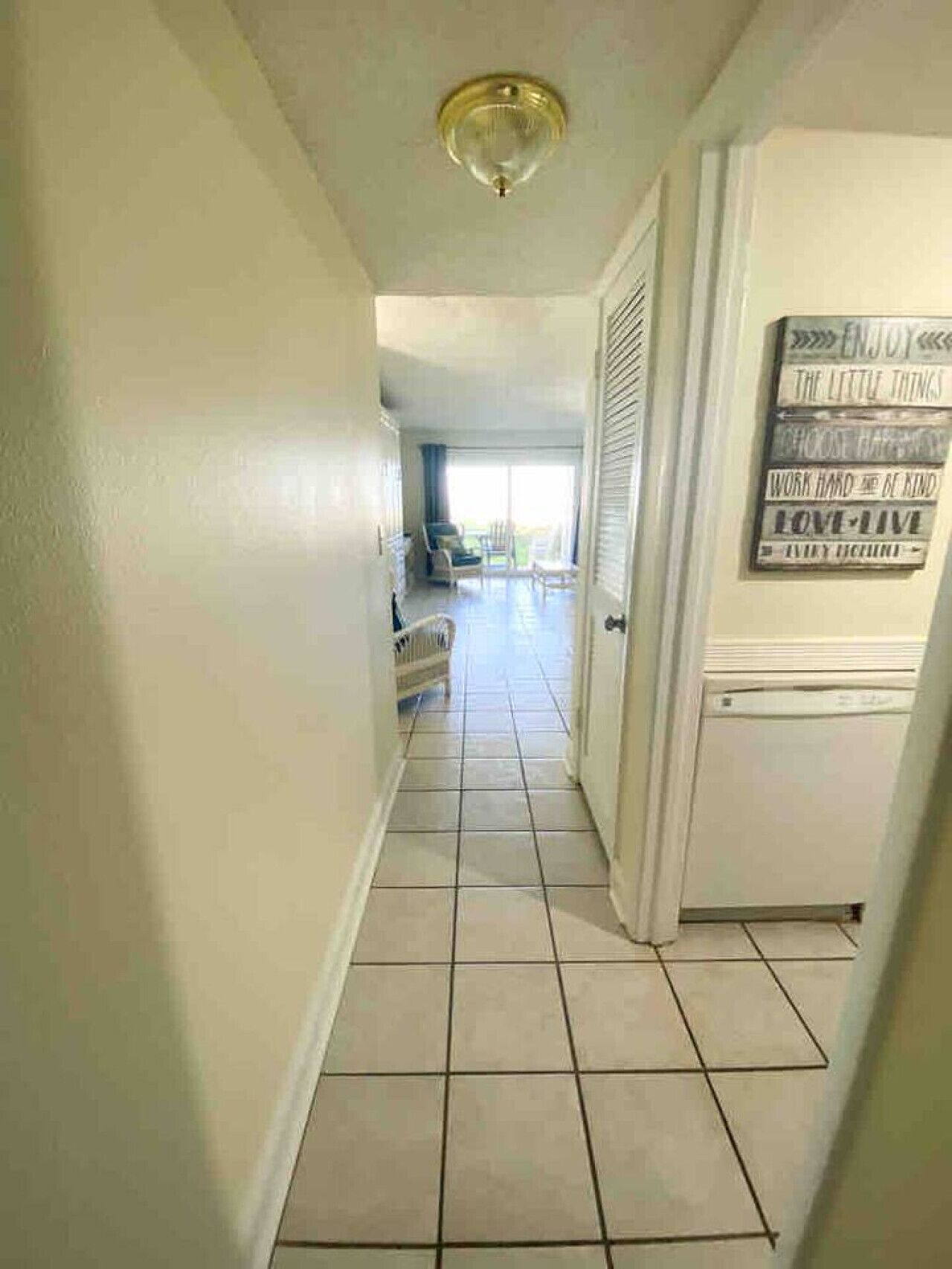 A hallway with a tiled floor leading to a room with a ceiling fan and a door with motivational signs.