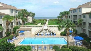 A pool area with lounge chairs and umbrellas, surrounded by palm trees and a view of the ocean. - Perfect located ocean front efficiency. (St. Augustine)