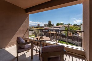 Un balcon avec deux chaises, une petite table et une boisson. Le balcon donne sur un quartier résidentiel avec des maisons et un ciel dégagé.
