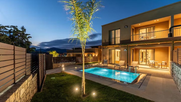 A modern two-story house with a swimming pool, a well-maintained lawn, and a stone wall.