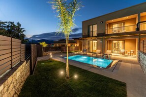Una casa moderna de dos pisos con piscina, césped cuidado y un muro de piedra.