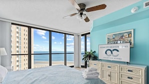 Un dormitori amb un llit gran, un ventilador de sostre, vista a la platja i un cartell de Ocean City Vacation Homes.