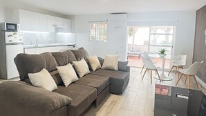 A modern living room with a sectional sofa, a dining area with white chairs, and a kitchen with white cabinets. - House With Private Terrace, Sunsets and Barbeque (Arona)