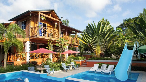 A wooden building with a balcony, a pool with lounge chairs, and a slide. - A 3-bedroom villa in beautiful San Francisco De Macoris with amenities and more (San Francisco De Macoris)