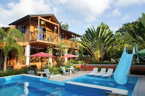 A wooden building with a balcony, a pool with lounge chairs, and a slide. - A 3-bedroom villa in beautiful San Francisco De Macoris with amenities and more (San Francisco De Macoris)