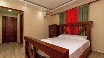 Een slaapkamer met een houten bed, nachtkastje, dressoir en een deur.