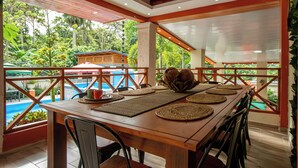 A wooden dining table with woven placemats, surrounded by chairs, overlooking a pool and lush greenery. - A 3-bedroom villa in beautiful San Francisco De Macoris with amenities and more (San Francisco De Macoris)