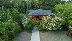 A house surrounded by lush greenery, with a gravel path leading to the entrance. - A 3-bedroom villa in beautiful San Francisco De Macoris with amenities and more (San Francisco De Macoris)