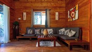 A wooden cabin interior with a sofa, a coffee table, and a window with curtains. - A 3-bedroom villa in beautiful San Francisco De Macoris with amenities and more (San Francisco De Macoris)