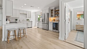 A spacious kitchen with white cabinetry, a central island with stools, and a view into the adjacent dining area.