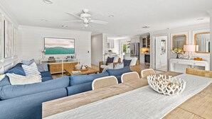 A modern living room with a blue sofa, a dining table with a white centerpiece, and a ceiling fan.
