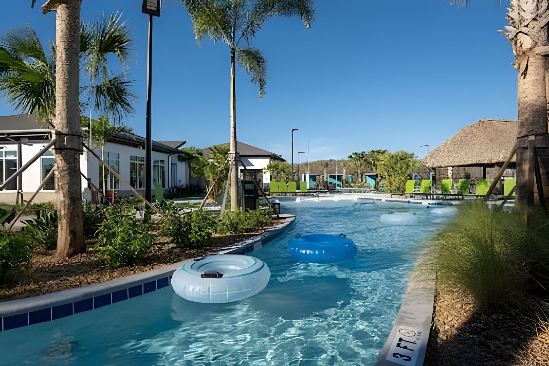A swimming pool with inflatable rings, surrounded by palm trees and buildings.
