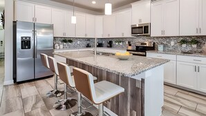 Une cuisine moderne avec des meubles blancs, un réfrigérateur en acier inoxydable, un plan de travail en granit et des tabourets de bar.