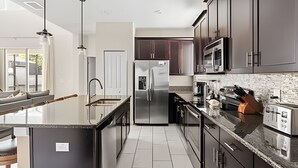 A modern kitchen with a central island, stainless steel appliances, dark cabinetry, and a large window providing natural light. - 5BR w/ South Pool, Game Room – Storey Lake (Kissimmee)
