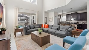 A spacious living area with a sectional sofa, a coffee table, and a blue armchair. - 5BR w/ South Pool, Game Room – Storey Lake (Kissimmee)