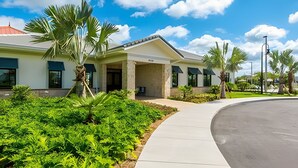 A modern building with a covered entrance, surrounded by lush greenery and palm trees. - 6BR Townhome w/ Pool – 10 Min to Disney (Kissimmee)