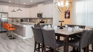 A modern kitchen with white cabinets, a central island, and a dining area with a table and chairs. - 6BR Townhome w/ Pool – 10 Min to Disney (Kissimmee)