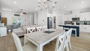 Een moderne keuken met witte kasten, een centraal eiland en een eethoek met een houten tafel en witte stoelen.