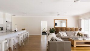 A modern living room with a sofa, a coffee table, and a kitchen area with a refrigerator and bar stools. - Casa Siena | In the Heart of the Hunter Valley (Pokolbin)