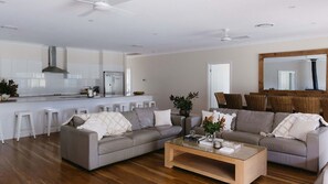 A modern living room with two sofas, a coffee table, and a kitchen area with white cabinets and a stainless steel refrigerator. - Casa Siena | In the Heart of the Hunter Valley (Pokolbin)
