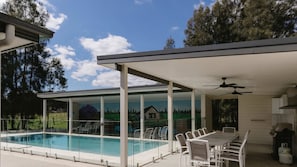A covered outdoor pool area with a dining table and chairs, surrounded by glass walls with a landscape mural.