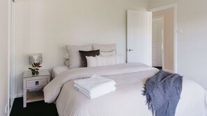 A neatly made bed with a gray throw blanket, a bedside table with a lamp, and a door to the right.