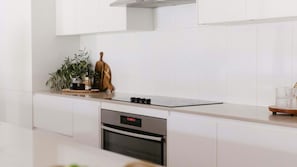 A modern kitchen with white cabinetry, a stainless steel oven, and a black induction cooktop.