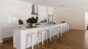 A modern kitchen with a central island, bar stools, and a stainless steel refrigerator. - Casa Siena | In the Heart of the Hunter Valley (Pokolbin)