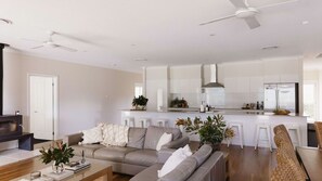 A modern living room with a sofa, coffee table, and a TV. A kitchen with white cabinets and a refrigerator is visible in the background. - Casa Siena | In the Heart of the Hunter Valley (Pokolbin)
