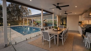A modern outdoor kitchen with a pool, dining area, and a view of the surrounding landscape. - Casa Siena | In the Heart of the Hunter Valley (Pokolbin)