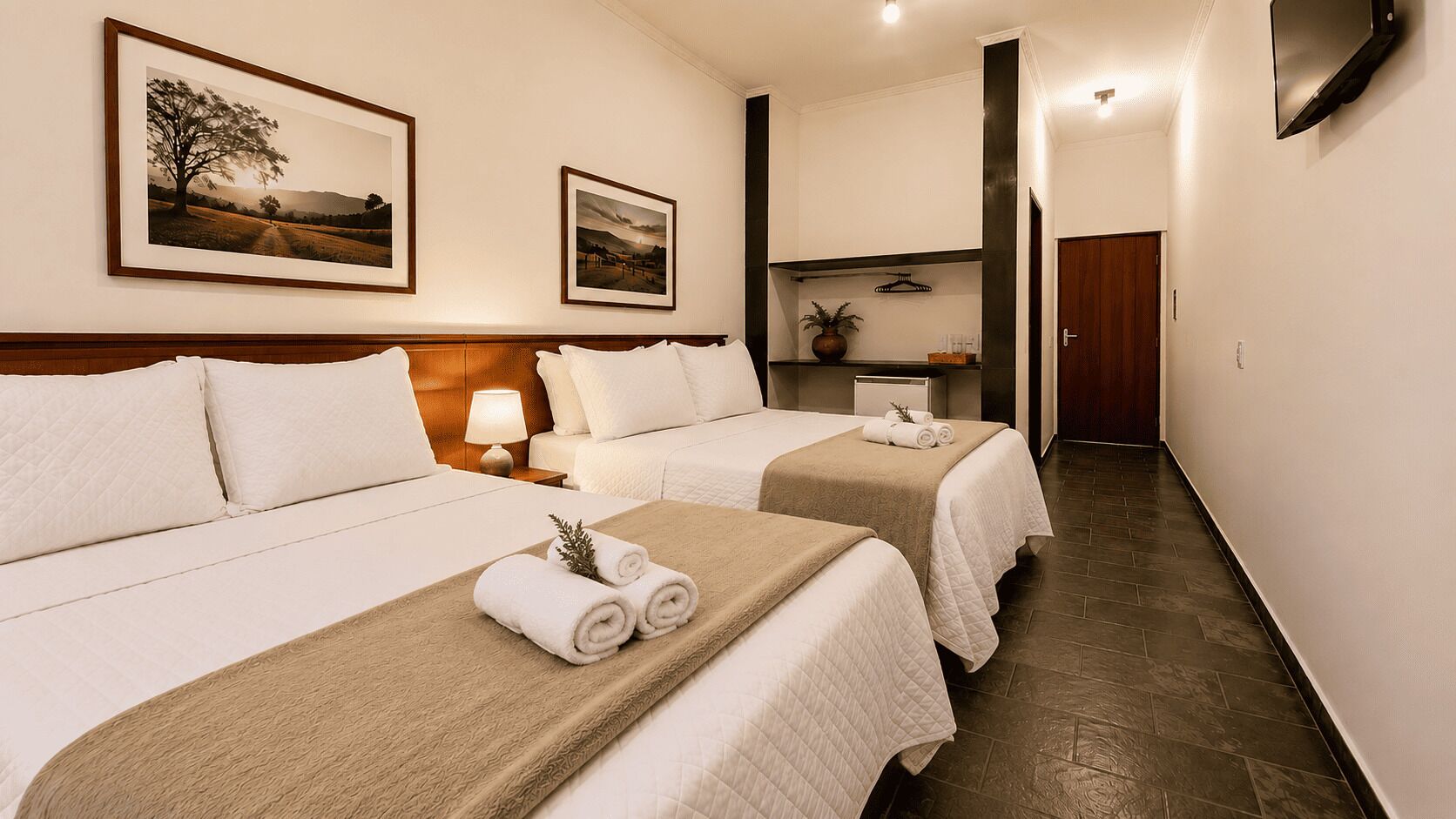 Habitación de hotel con dos camas, una mesita de noche, una lámpara y un cuadro enmarcado en la pared.