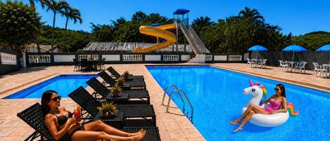A swimming pool with lounge chairs, a water slide, and a unicorn float.