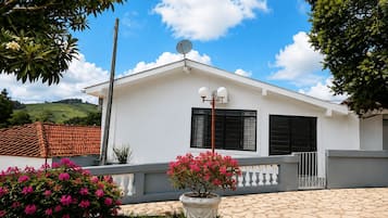 Um edifício branco com antena parabólica, persianas pretas e entrada com calçada de pedra.