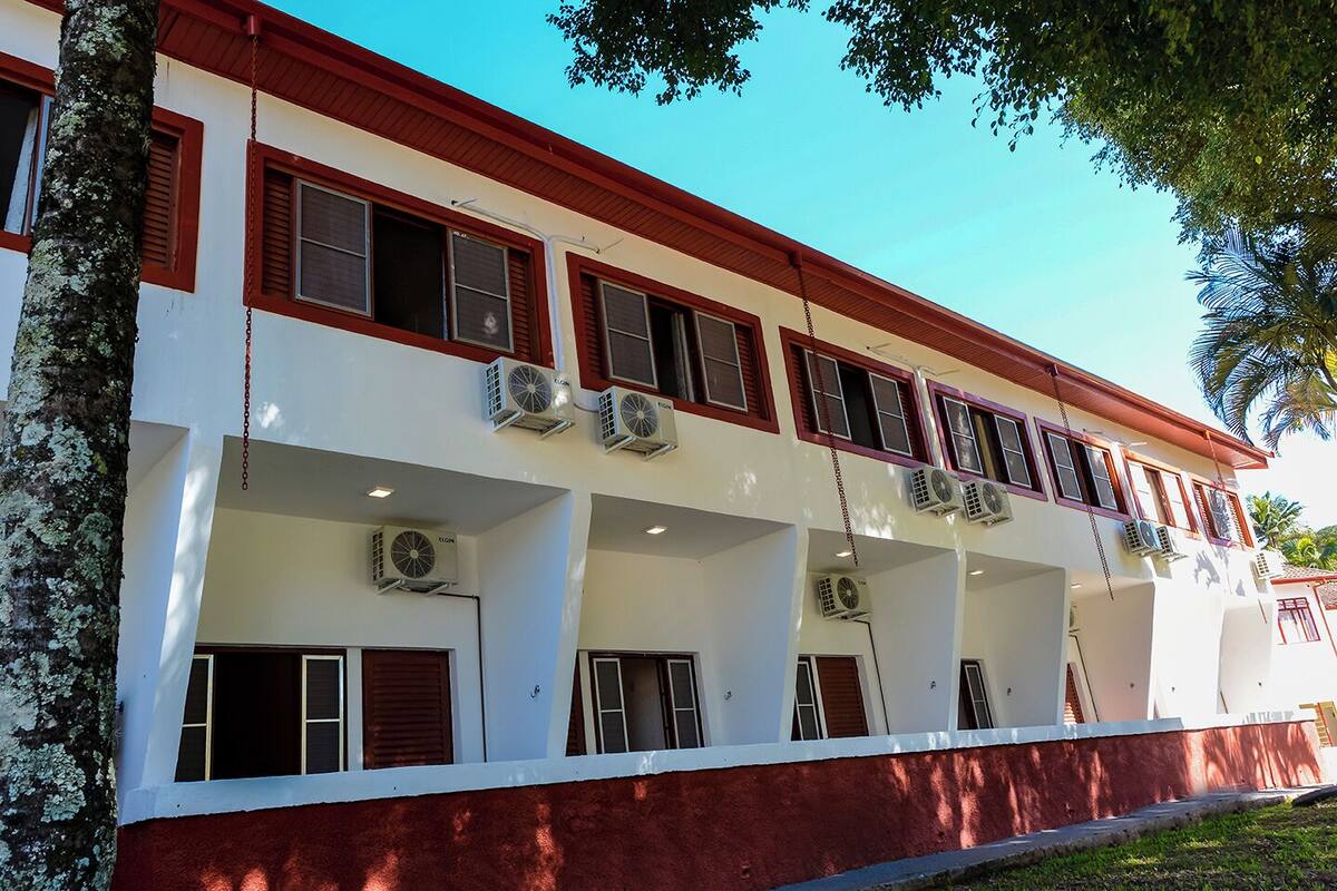 Ein mehrstöckiges Gebäude mit roter und weißer Fassade, mehreren Klimaanlagen und einer Reihe von Fenstern mit Rollläden.