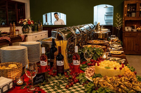 A buffet table with various food items, wine bottles, and a television screen in the background.