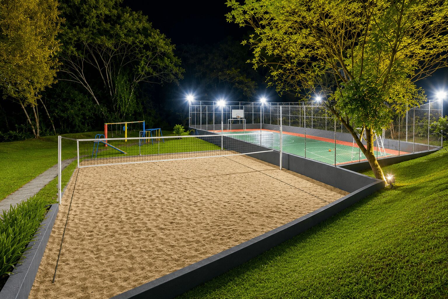 Instalación deportiva exterior bien iluminada con una cancha de voleibol de playa y una cancha de tenis, rodeada de árboles y una valla.