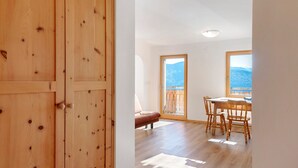 Una porta de fusta, una taula de dinar amb caires, un sofà i una vista de muntanyes a través d'una finestra.