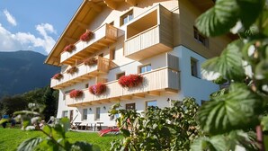 Un edifici de diverses plantes amb balcons, un terrat pla i un paisatge de muntanyes al fons.