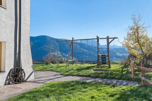 A stone pathway leading to a wooden swing set in a grassy area with a mountain backdrop.