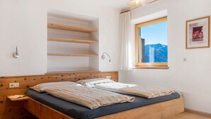 A bedroom with a wooden bed, built-in shelves, a window with a mountain view, and a wall-mounted light fixture. - Apartment 'Zolerhof Anemone' with Mountain View, Shared Terrace and Wi-Fi (Feldthurns)