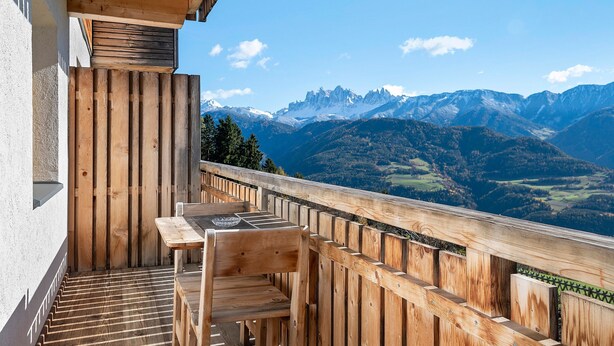 A wooden balcony with a table and chairs, overlooking a mountainous landscape. - Apartment 'Zolerhof Anemone' with Mountain View, Shared Terrace and Wi-Fi (Feldthurns)