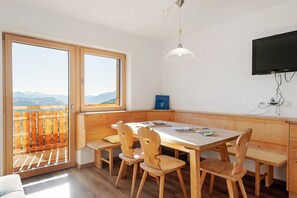 Een kamer met een houten tafel en stoelen, een bank, een televisie en uitzicht door grote ramen.