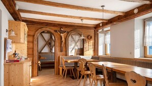 A wooden interior with a long table and chairs, a wooden counter, and arched windows.