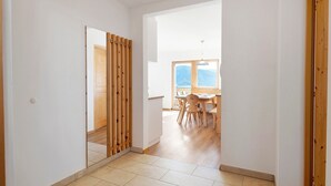 A hallway with a wooden partition, a dining area with a table and chairs, and a view through a window.