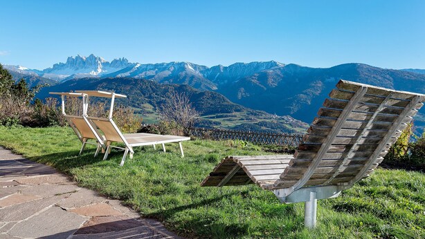 Un espace verdoyant avec deux chaises longues et une table, offrant une vue sur une chaîne de montagnes.