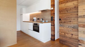 Une cuisine compacte avec des meubles blancs, un mur d’accent en bois et un four encastré.